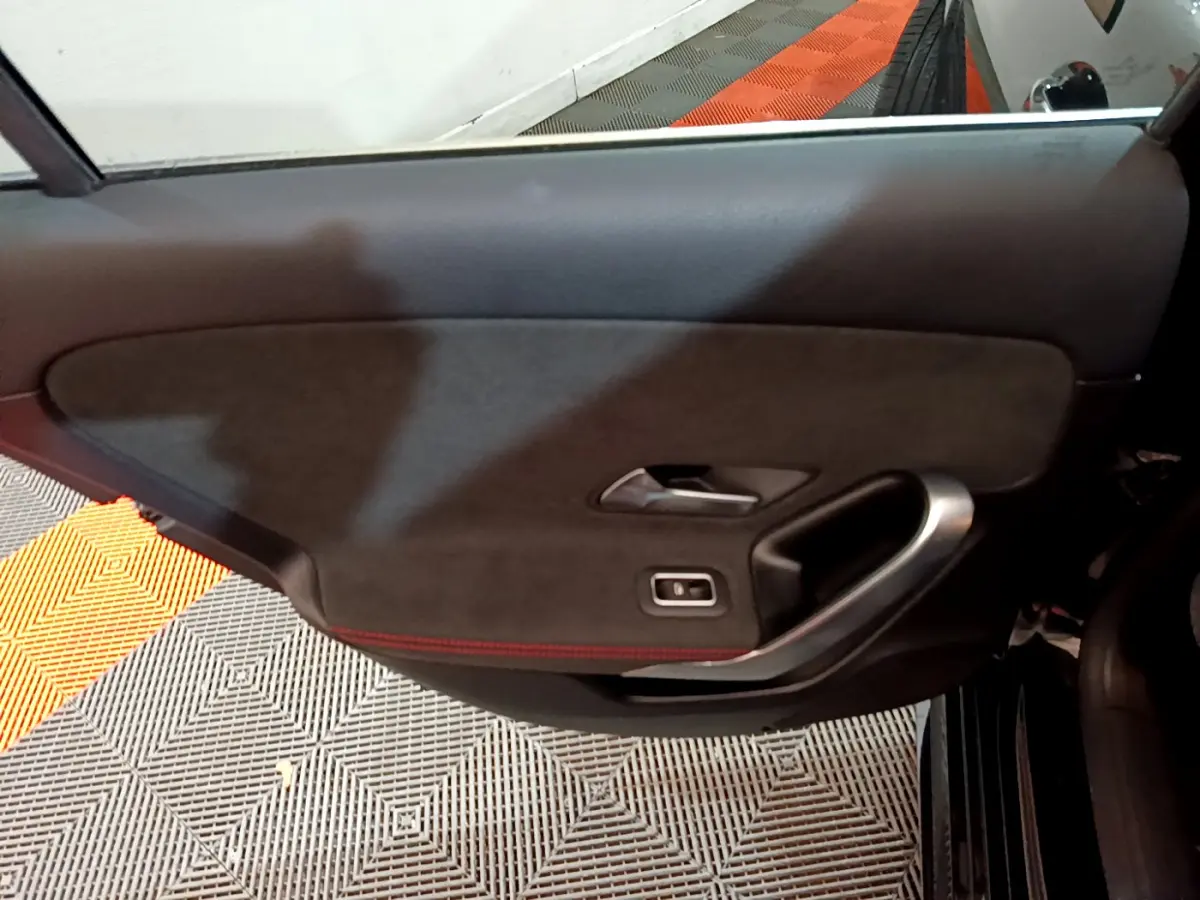 Gros plan sur la porte intérieure côté gauche noire avec surpiqûres rouges et poignée alu de la Mercedes Classe A 180 AMG Line.