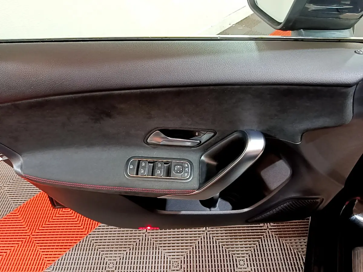Gros plan sur la porte côté gauche d'une Mercedes Classe A 180 AMG Line noire, avec commandes de vitres et poignée alu.