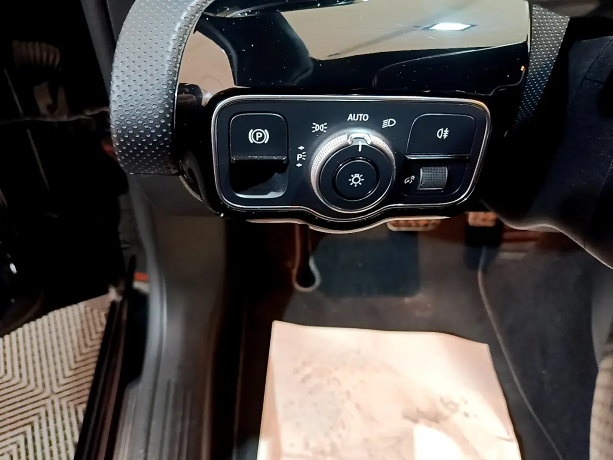 Gros plan sur la commande des phares et frein à main électrique dans l'habitacle noir d'une Mercedes Classe A 180 AMG Line.