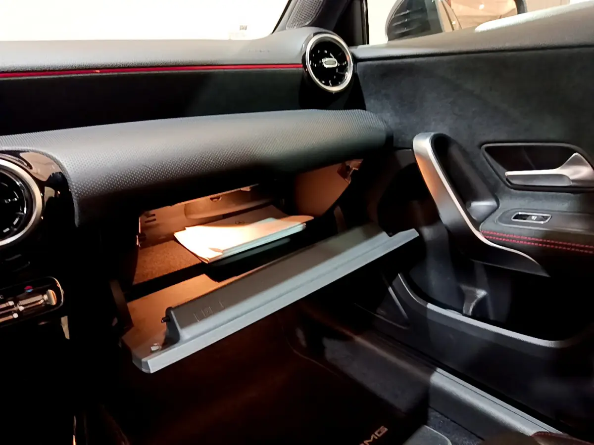 Intérieur de la Mercedes Classe A 180 AMG Line 2019, vue côté passager avec boîte à gants ouverte et détails en noir et rouge.