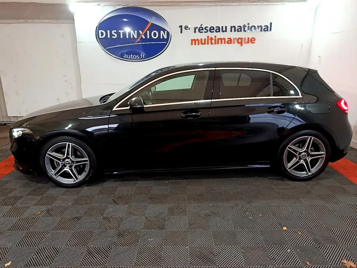 Profil droit d'une Mercedes Classe A 180 AMG Line noire, avec jantes alliage et feux arrière allumés dans un showroom.