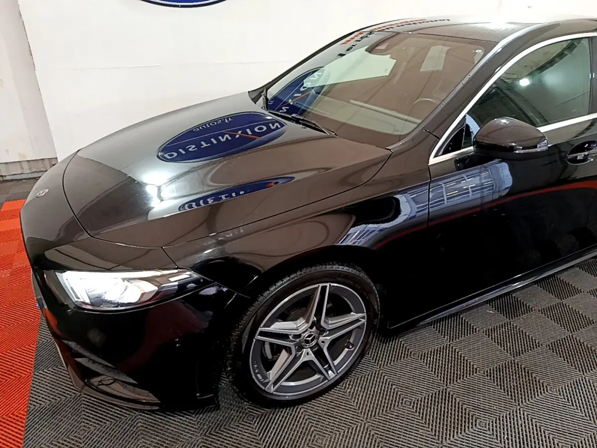 Mercedes Classe A 180 AMG Line noire vue en 3/4 avant droit, avec jantes alliage et phares LED allumés.