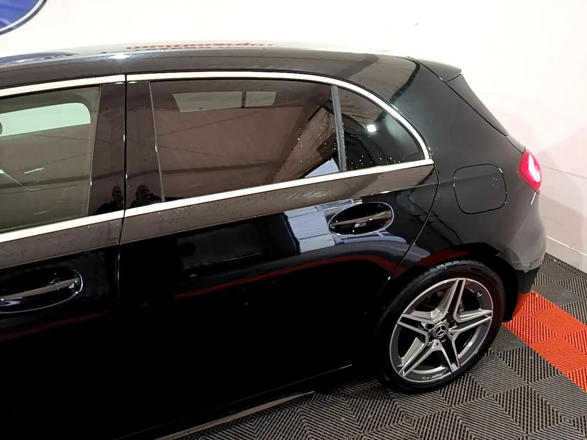 Vue latérale droite d'une Mercedes Classe A 180 AMG Line noire, mettant en valeur la jante alliage et la ligne de toit chromée.