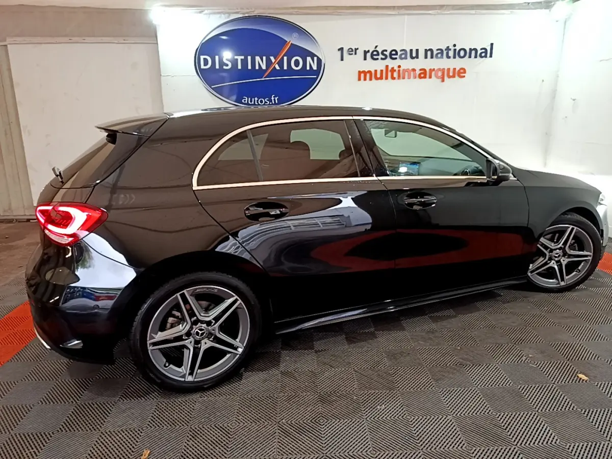 Vue de profil côté droit d'une Mercedes Classe A 180 AMG Line noire avec jantes alliage et feux arrière LED allumés.