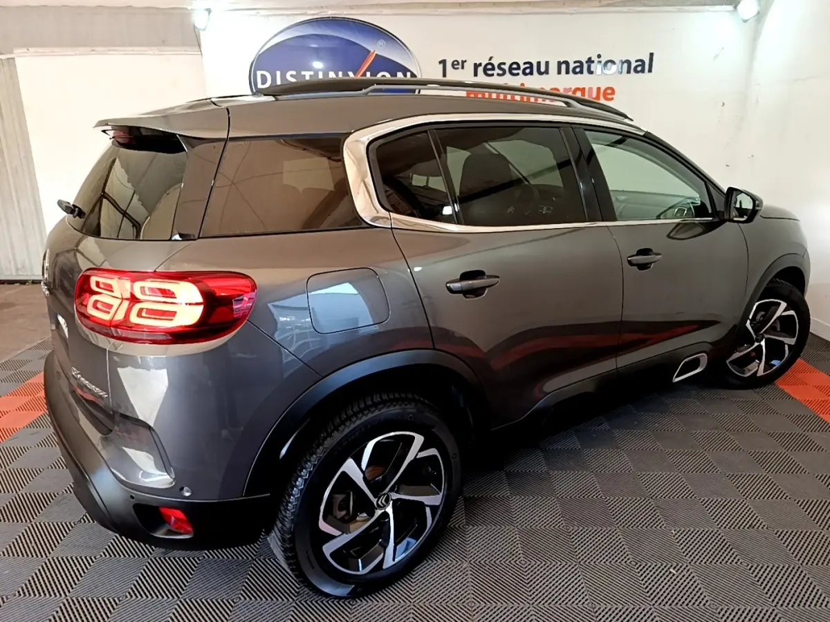 Vue 3/4 arrière droite d'un Citroën C5 Aircross gris foncé avec feux arrière LED allumés et jantes bicolores.