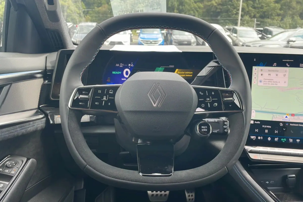 Vue centrée sur le volant en cuir noir avec logo Renault, tableau de bord numérique et écran tactile du Renault Austral gris schiste.