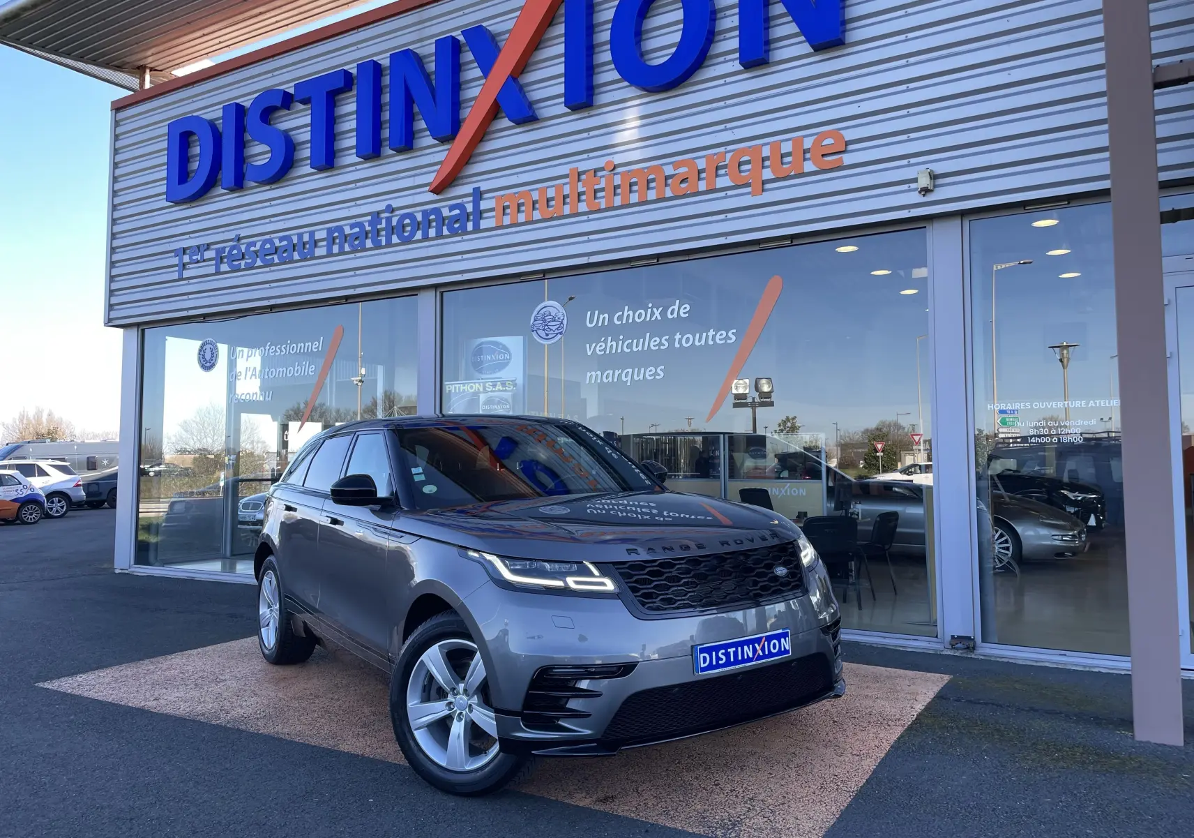Range Rover Velar D240 S R-Dynamic gris Corris en 3/4 avant droit devant un showroom Distinxion.
