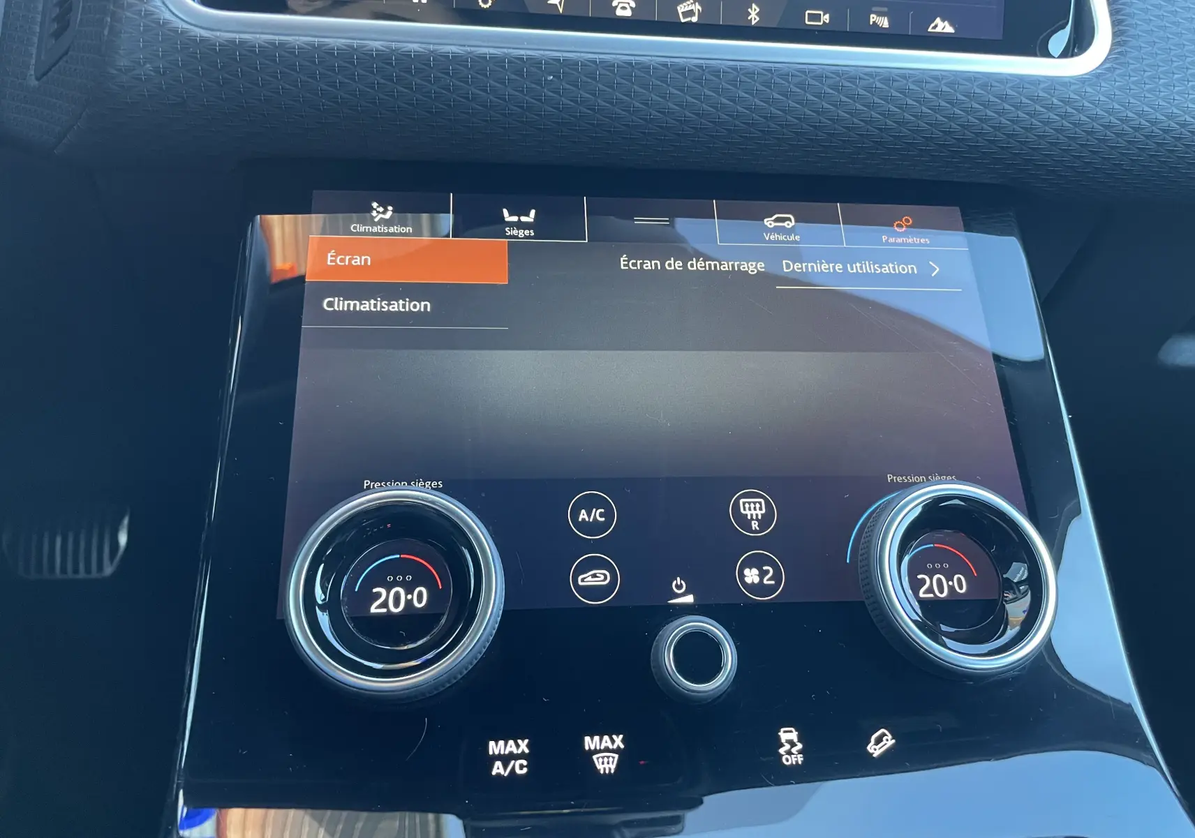 Gros plan sur la console centrale tactile du Range Rover Velar gris, affichant la climatisation réglée à 20°C des deux côtés.