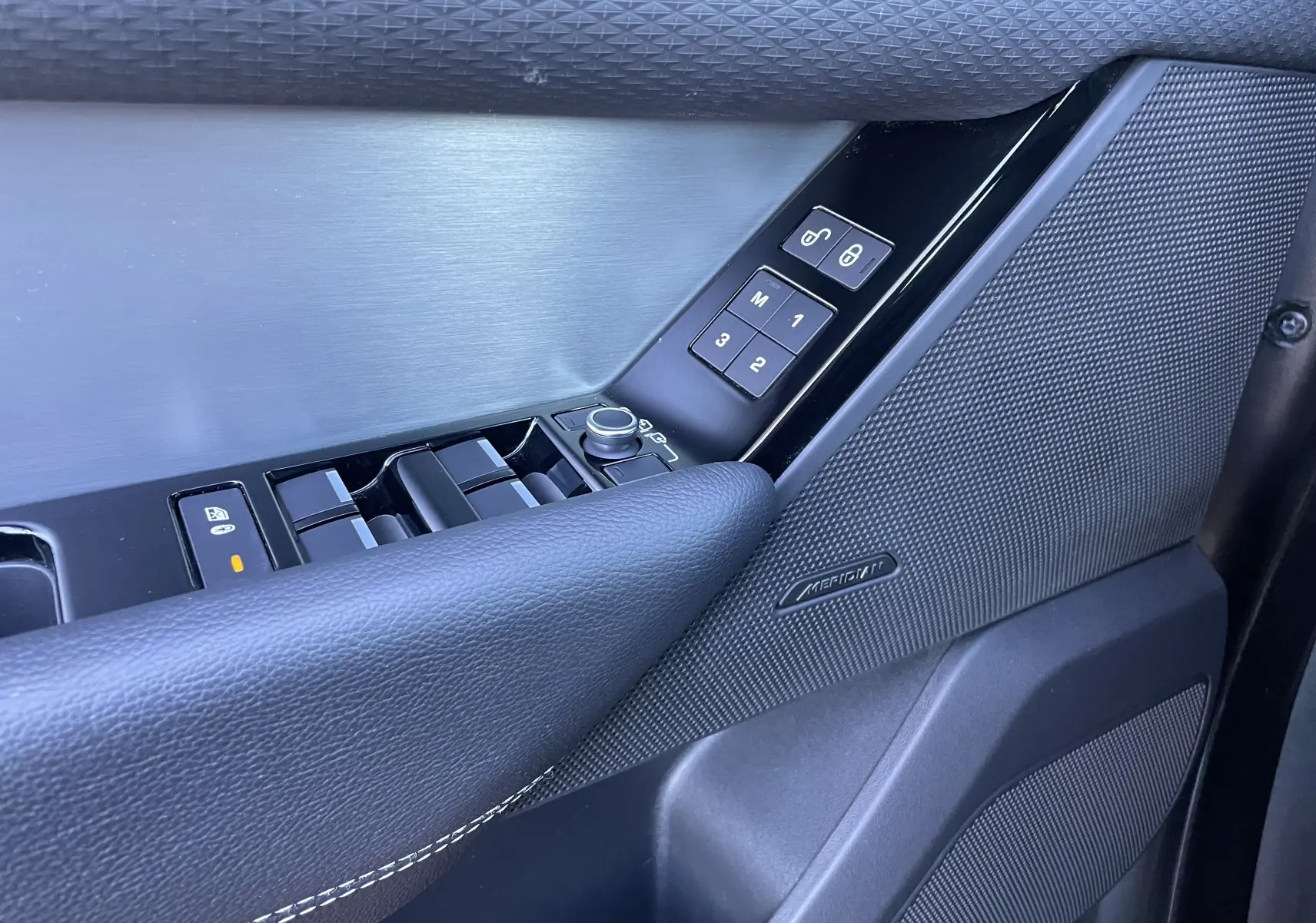 Gros plan sur la porte côté gauche du Range Rover Velar gris, avec commandes de vitres et haut-parleur Meridian.