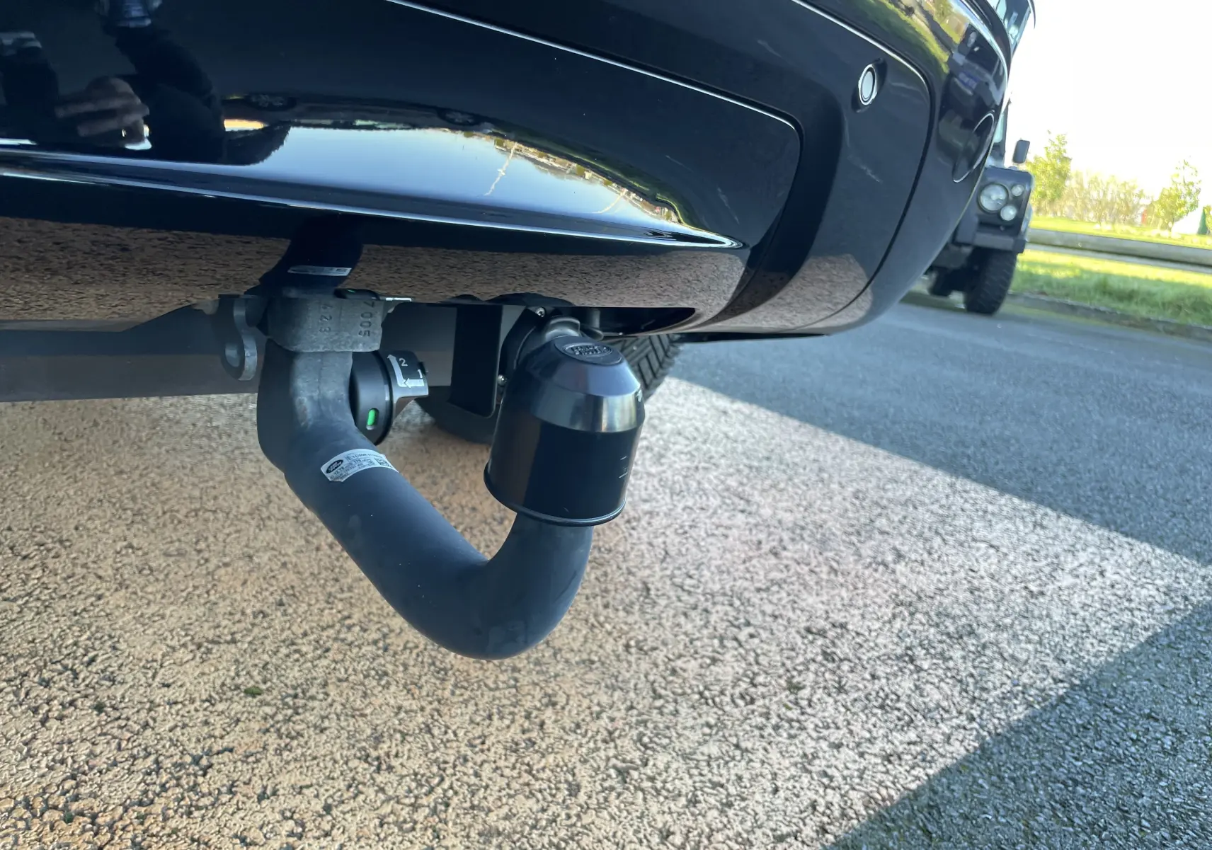 Gros plan sur l'attelage de remorque fixé à l'arrière d'un Range Rover Velar gris Corris, sous le pare-chocs noir brillant.