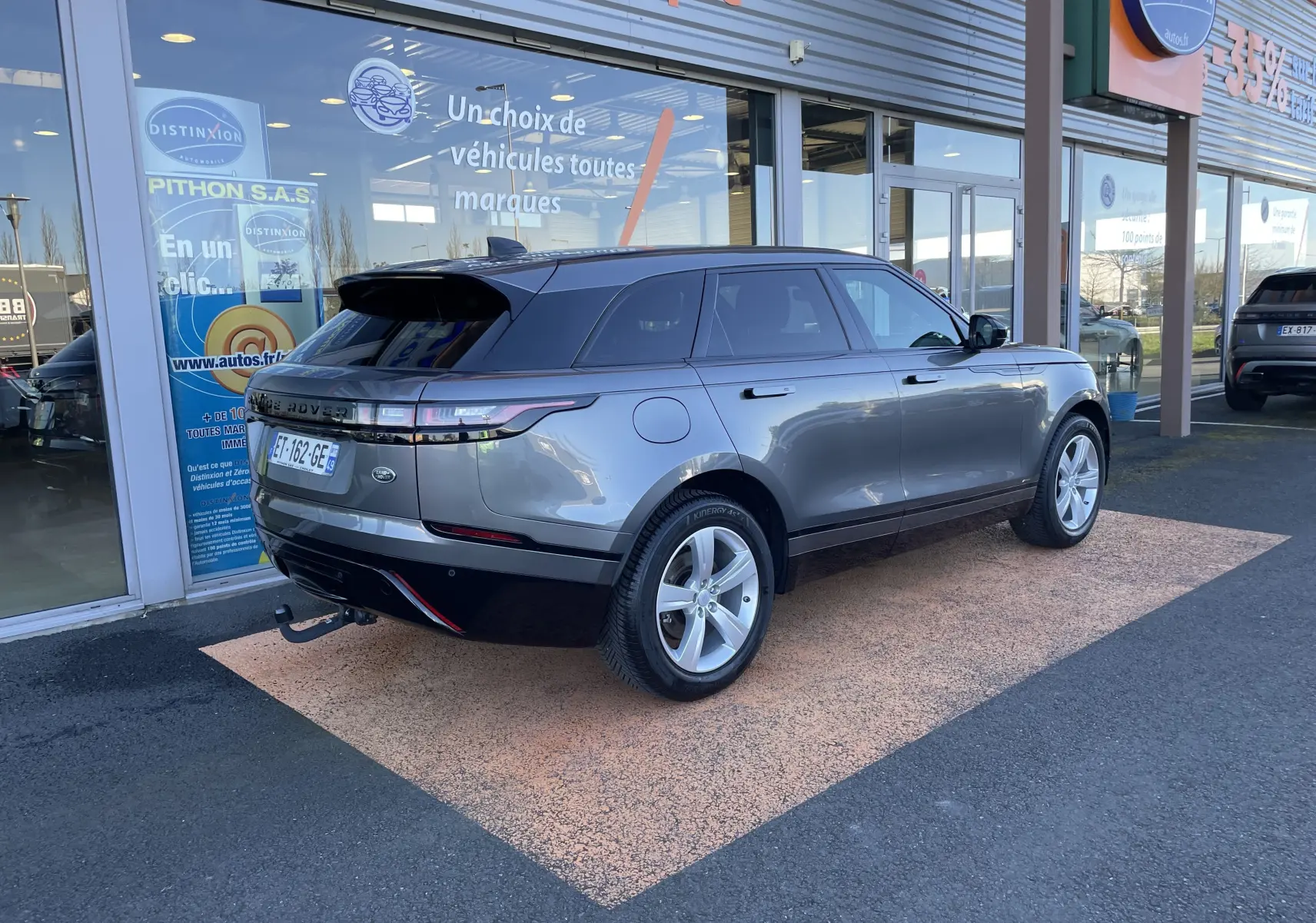 Range Rover Velar D240 S R-Dynamic gris Corris, vue 3/4 arrière droit, avec attelage et jantes argentées.