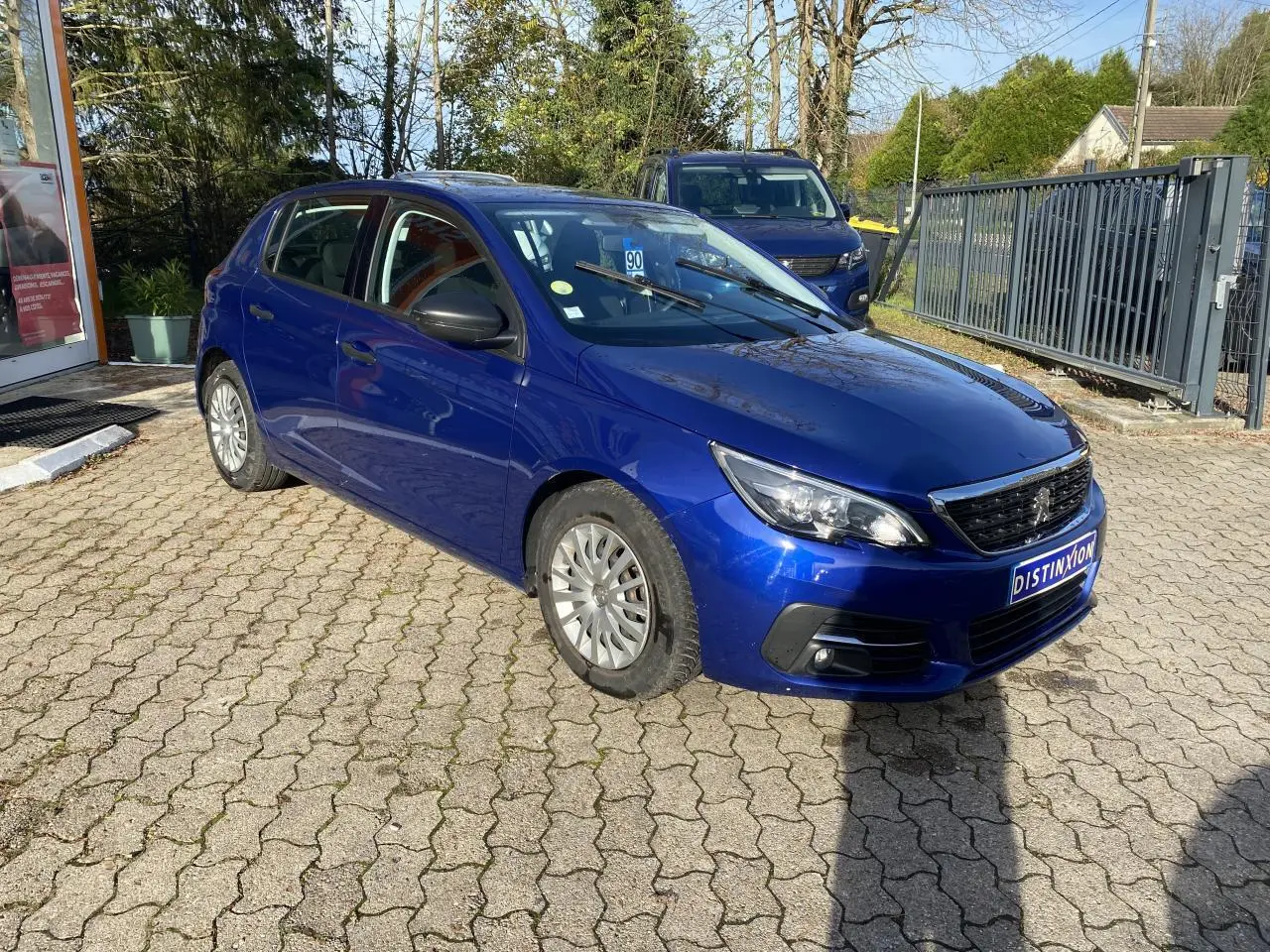 Peugeot 308 bleu foncé vue en 3/4 avant droit, avec projecteurs antibrouillard et jantes acier.