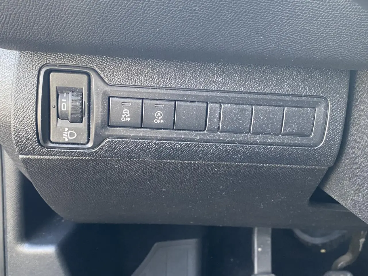 Gros plan sur les commandes de réglage des phares et des aides à la conduite sur la planche de bord noire d'une Peugeot 308 bleu foncé.