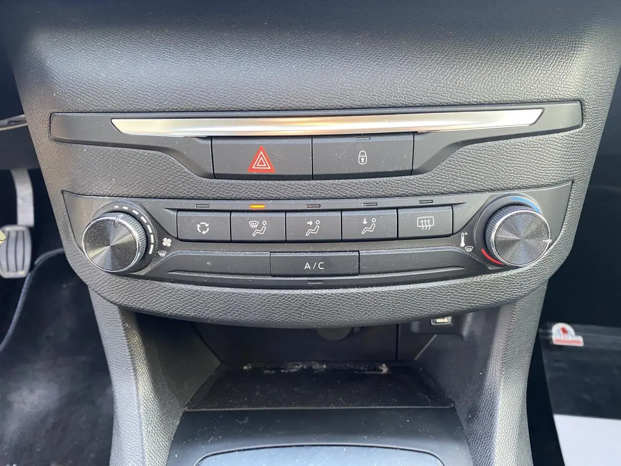 Vue rapprochée de la console centrale de la Peugeot 308 bleu foncé, montrant les commandes de climatisation et les boutons d'alerte.