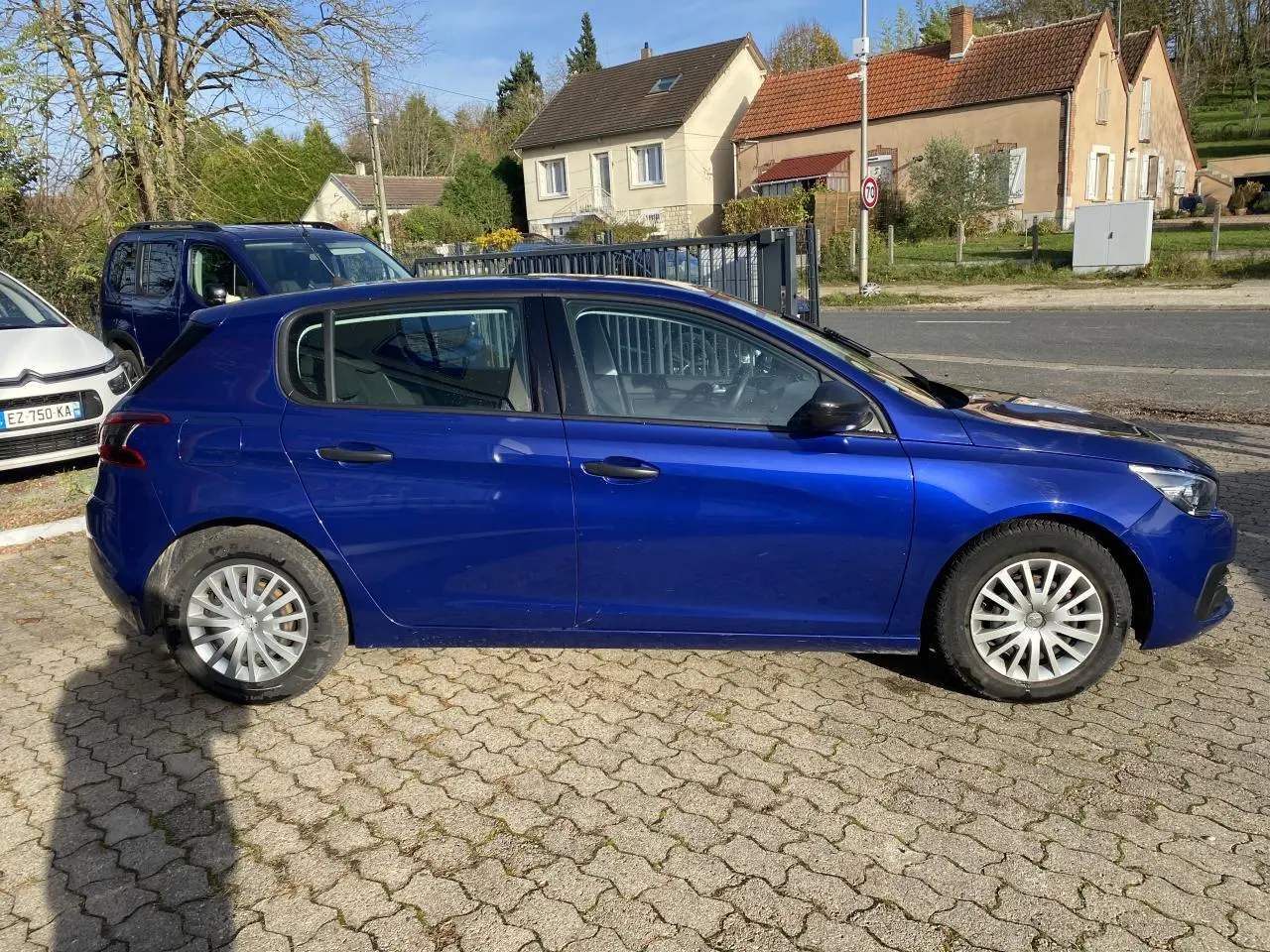 Peugeot 308 bleu foncé vue de profil côté gauche, stationnée sur un sol pavé avec roues en alliage.