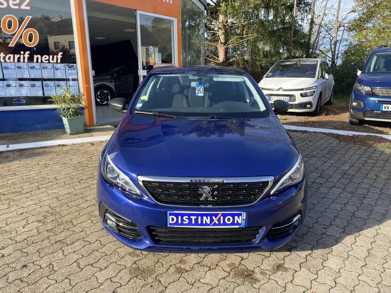 Peugeot 308 bleu foncé vue de face, avec calandre chromée et projecteurs antibrouillard halogènes visibles.
