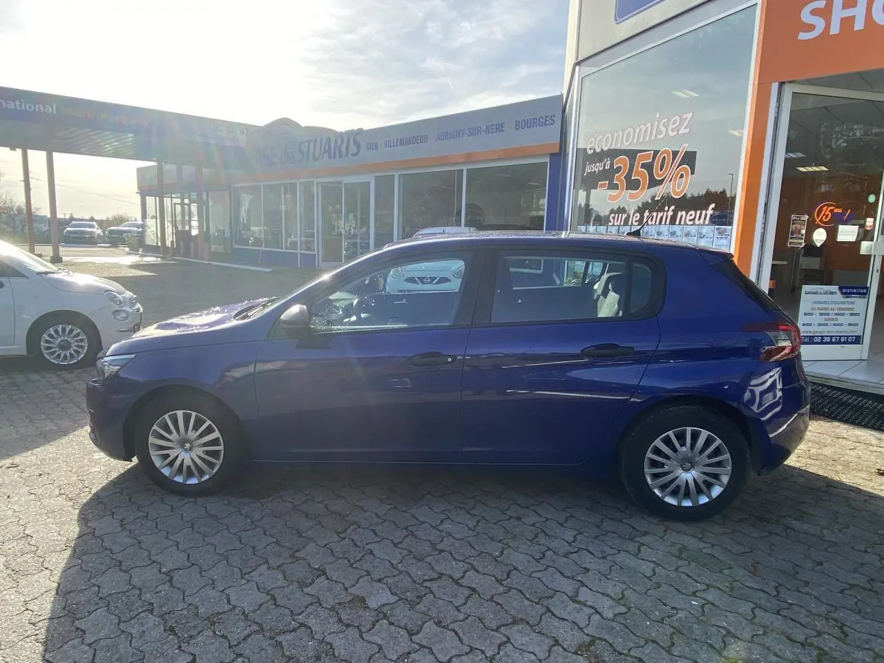 Profil côté gauche d'une Peugeot 308 bleu foncé garée devant un showroom avec jantes alliage simples.