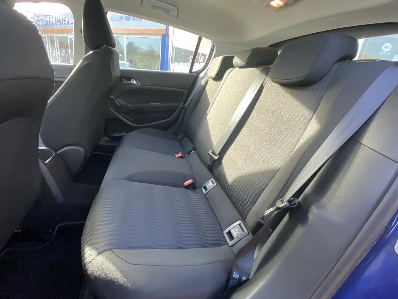 Vue intérieure côté droit de la banquette arrière noire d'une Peugeot 308 2017 bleu foncé avec ceintures de sécurité visibles.