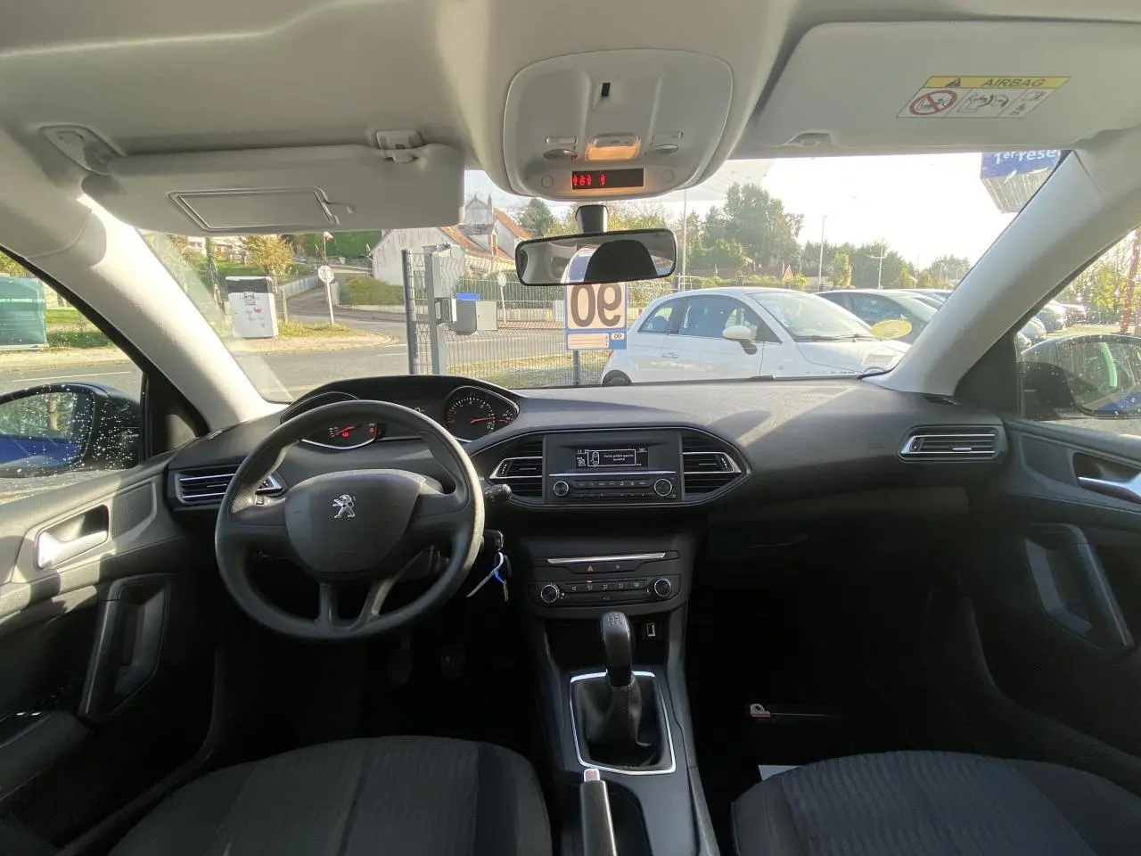 Vue intérieure avant de la Peugeot 308 2017, tableau de bord et volant noir avec boîte manuelle visible.