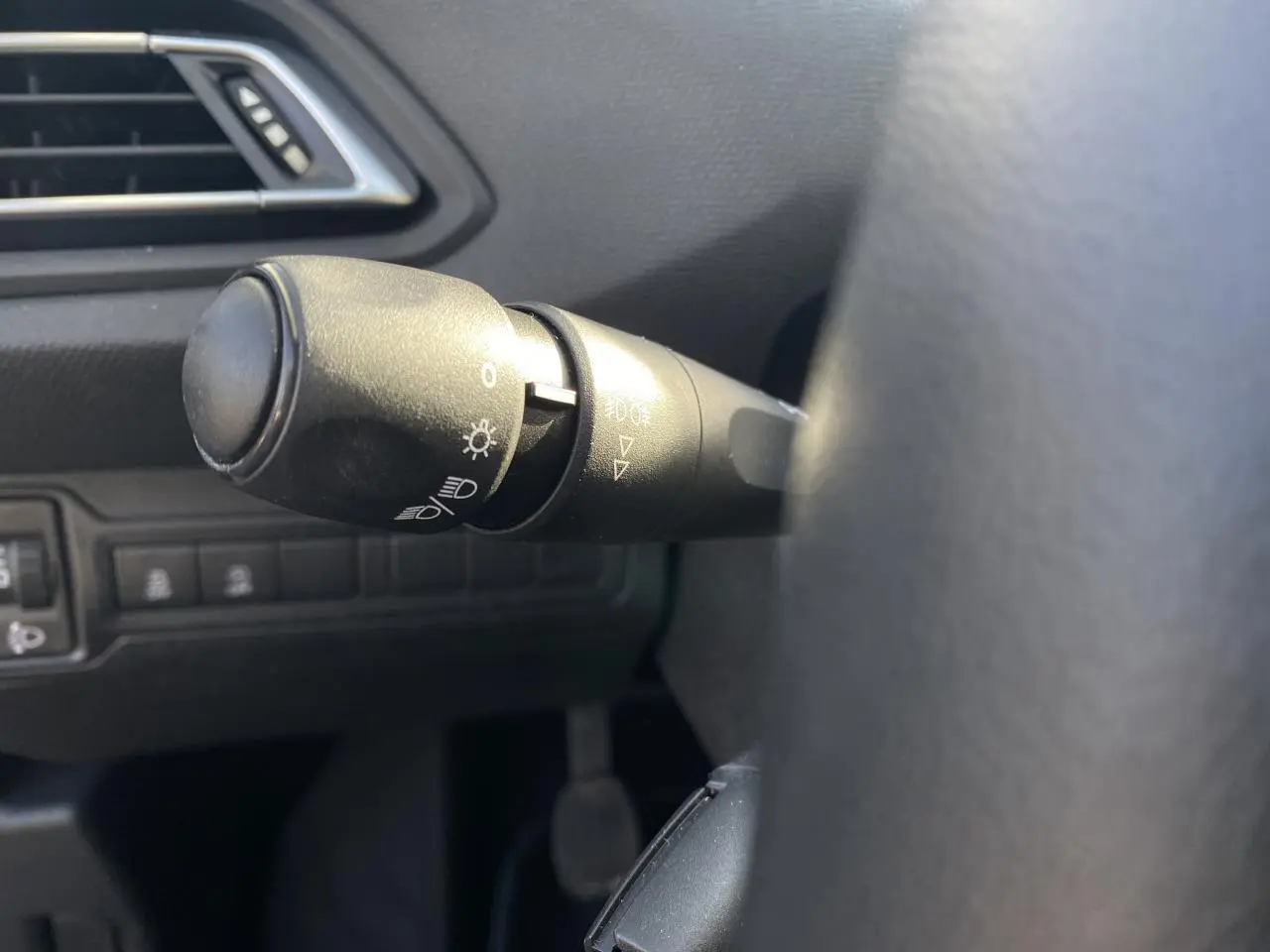 Gros plan sur la commande des phares à gauche du volant dans l'habitacle sombre d'une Peugeot 308 bleu foncé de 2017.