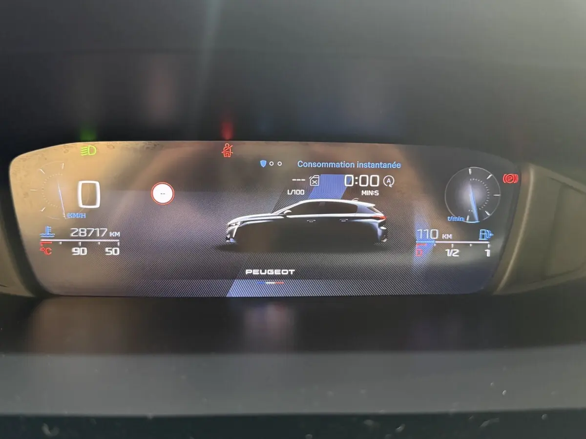 Affichage numérique du tableau de bord de la Peugeot 308 bleu, montrant silhouette du véhicule et données de consommation instantanée.