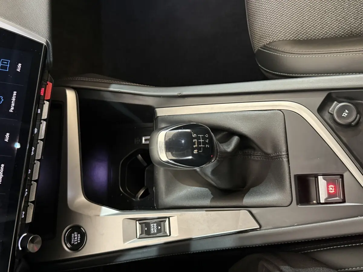 Vue plongeante sur la console centrale de la Peugeot 308 bleu, mettant en valeur le levier de vitesse manuel et le bouton start/stop.