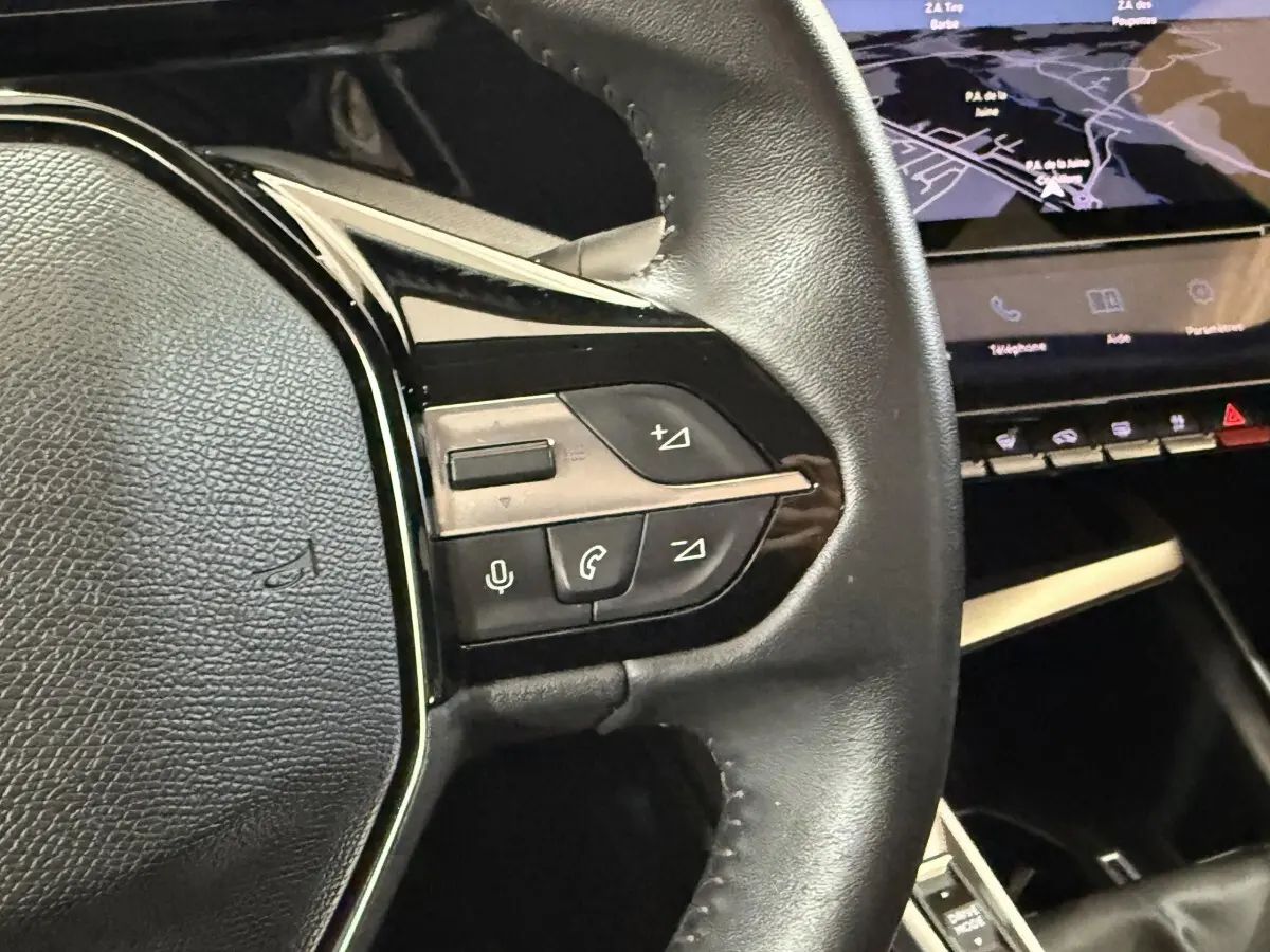 Gros plan sur le volant cuir noir de la Peugeot 308 2023 avec commandes vocales et écran tactile de navigation visible.