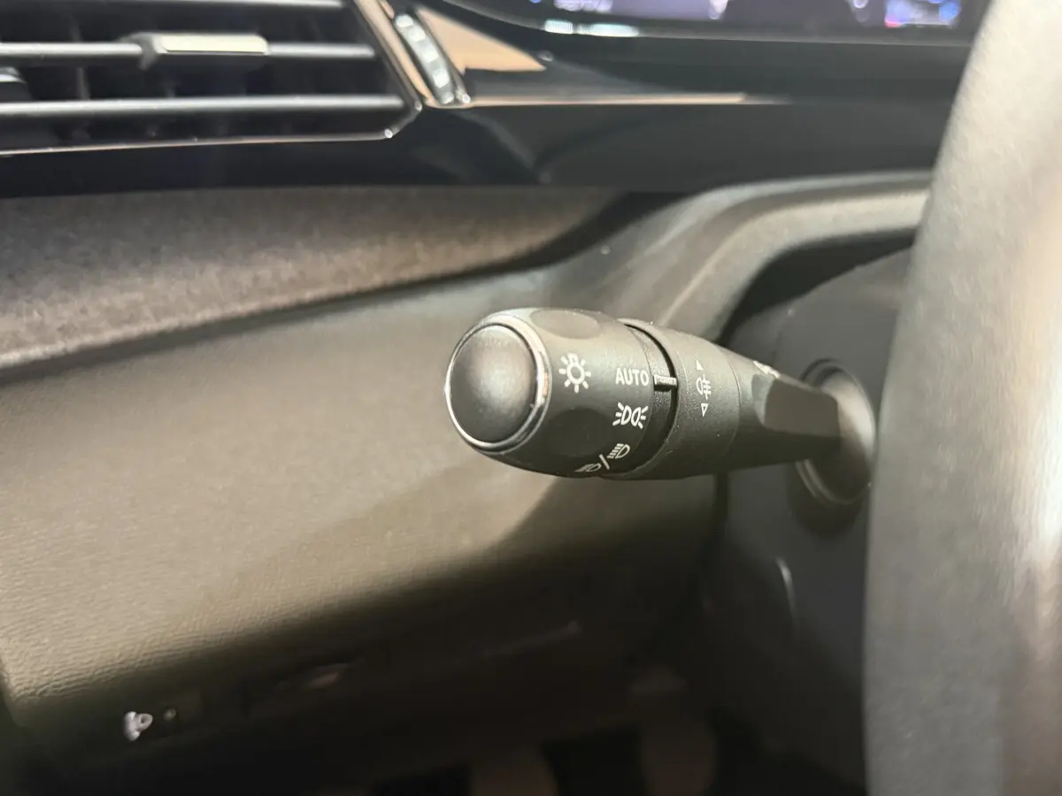 Gros plan sur la commande d'éclairage à gauche du volant dans l'habitacle sombre d'une Peugeot 308 2023 bleu.