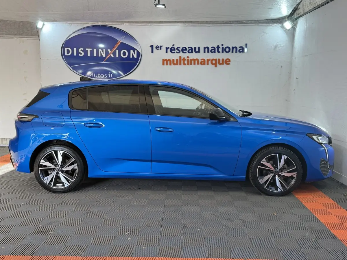 Profil droit d'une Peugeot 308 PureTech 130 bleu vif, avec jantes alliage et vitres teintées, en intérieur showroom.