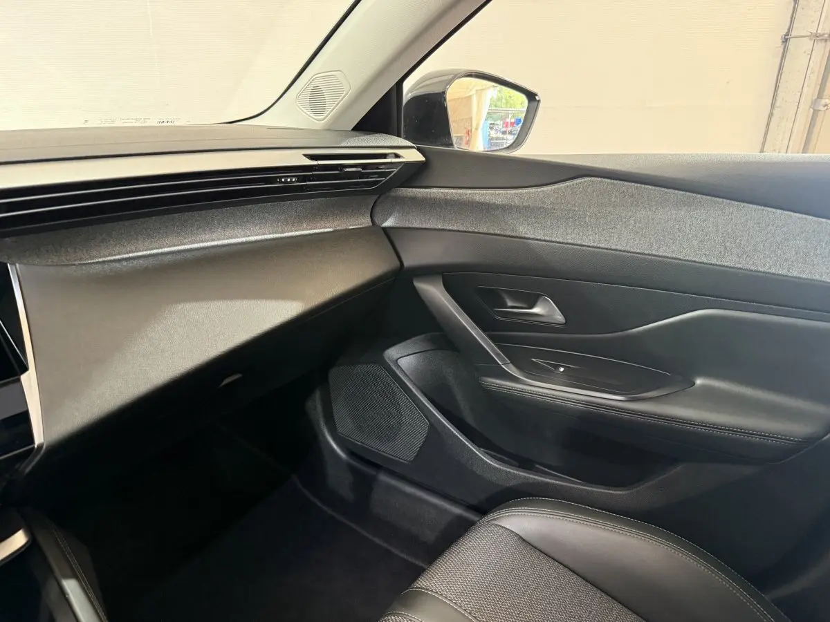 Vue intérieure côté passager de la Peugeot 308 2023, tableau de bord et porte en noir avec insert tissu gris.