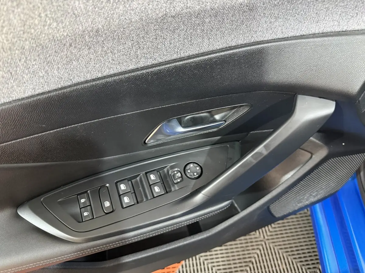 Vue intérieure côté gauche de la porte d’une Peugeot 308 bleu 2023, avec commandes des vitres et rétroviseurs électriques.