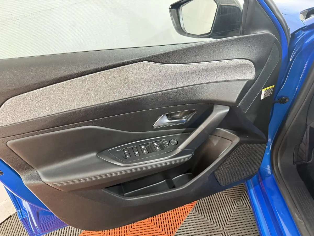 Vue rapprochée de la porte avant gauche bleu vif d'une Peugeot 308 2023 avec commandes électriques et garniture grise.
