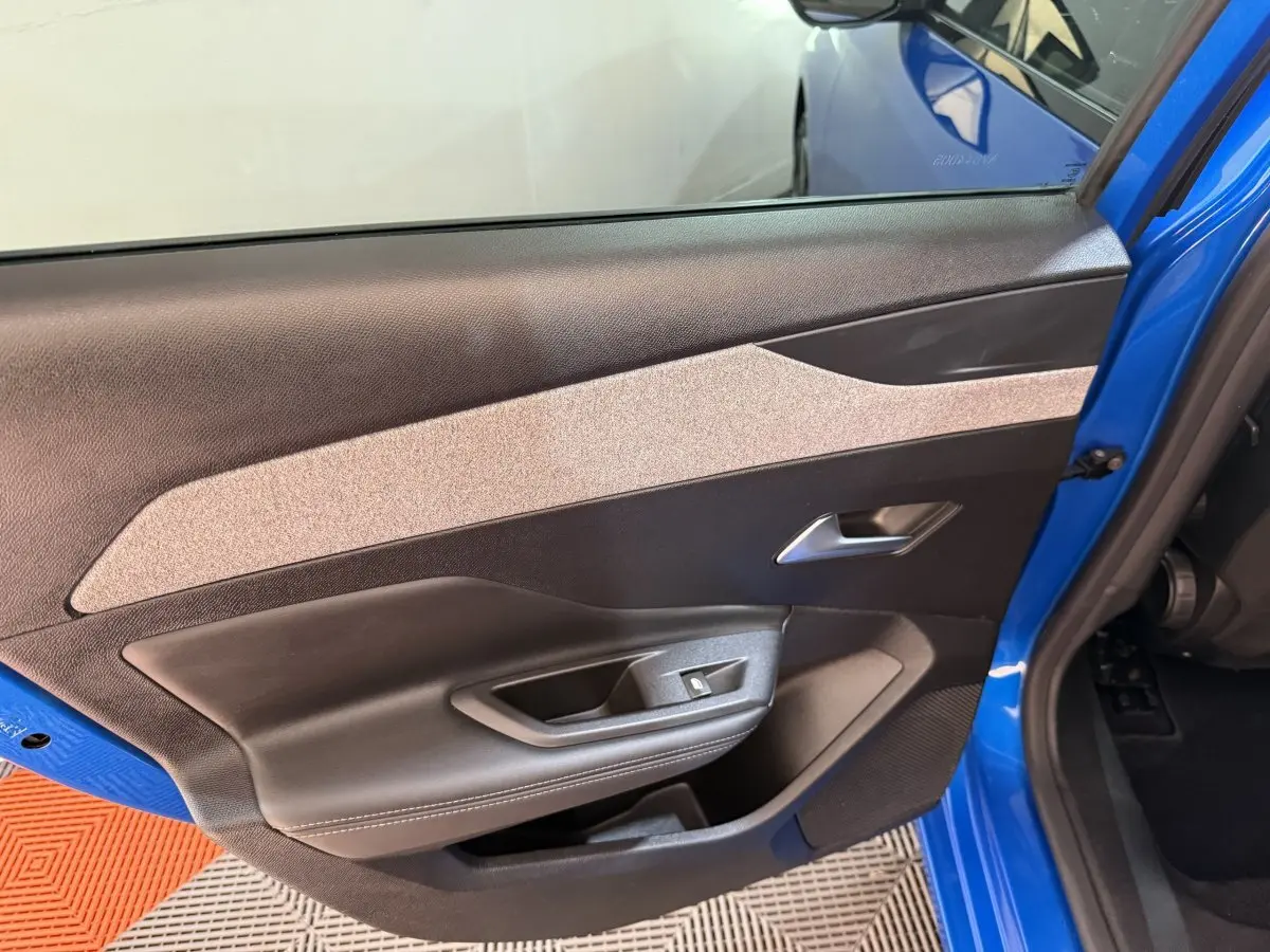 Vue intérieure de la porte avant gauche bleu vif d'une Peugeot 308 2023 avec garniture noire et beige.