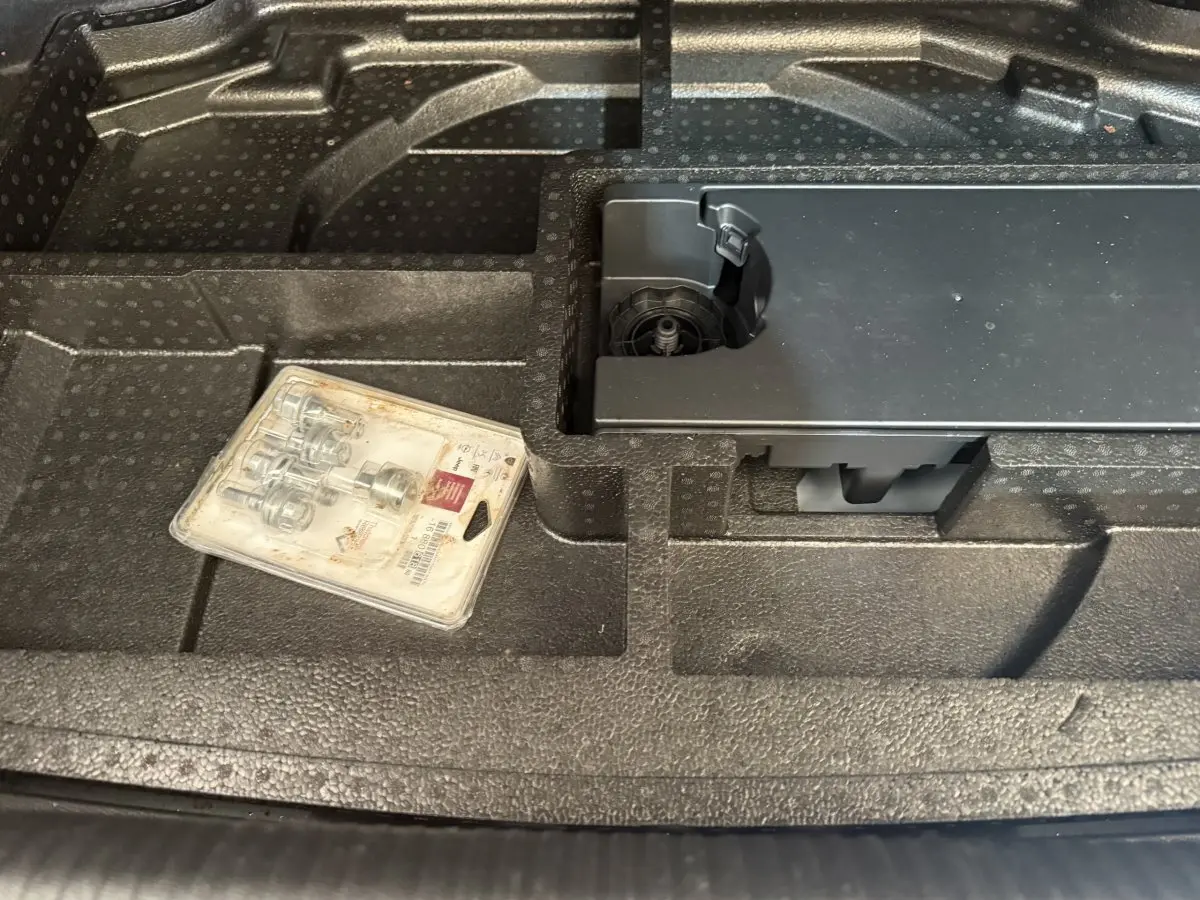 Gros plan sur le rangement en mousse noire du coffre d'une Peugeot 308 bleu, avec un kit de visserie posé dessus.