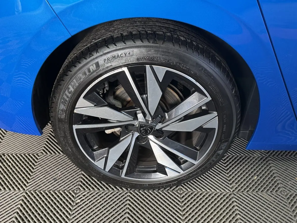 Gros plan sur la roue avant gauche d'une Peugeot 308 bleu 2023, jante alliage au design moderne et pneu Michelin.