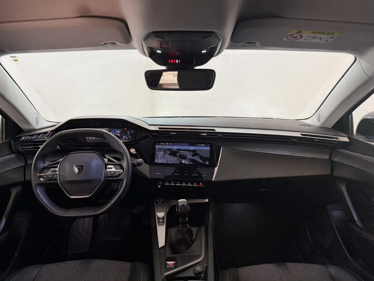 Intérieur avant de la Peugeot 308 PureTech 130 S&S Allure Pack 2023, tableau de bord noir avec écran tactile central et volant cuir.