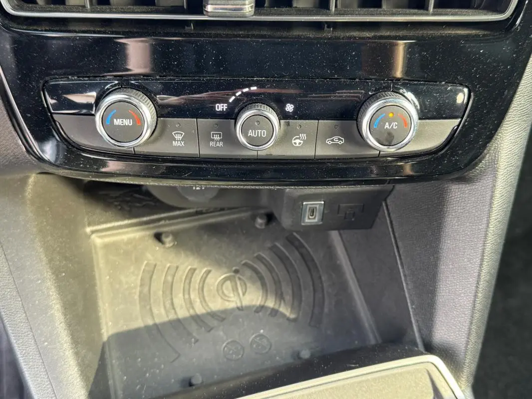 Gros plan sur la console centrale de l'Opel Mokka électrique 2025, montrant les commandes de climatisation et un espace de recharge sans fil.