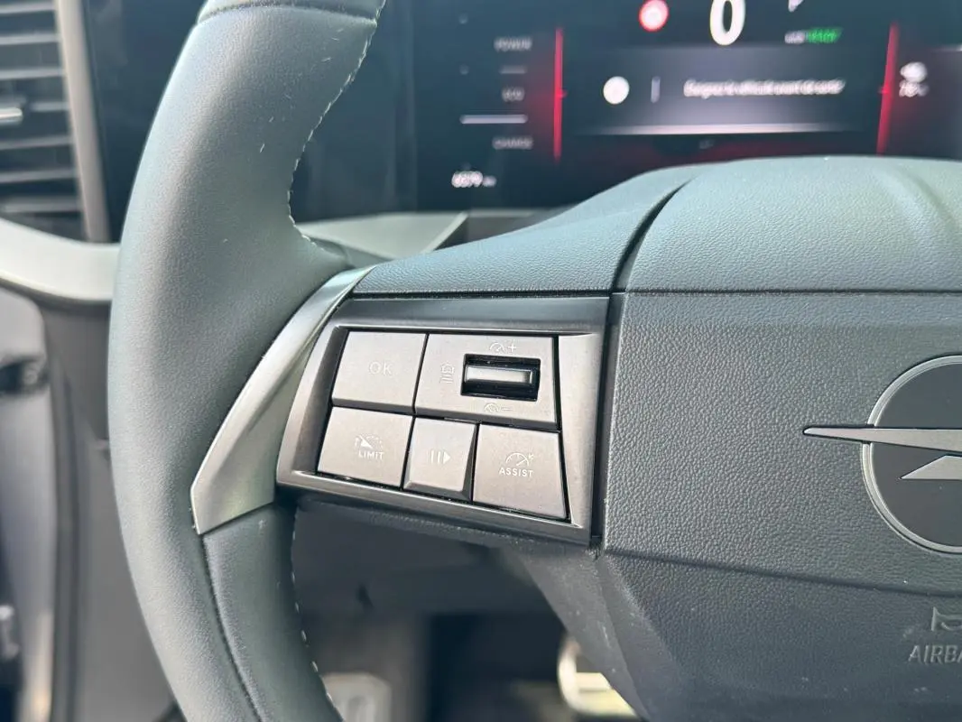 Gros plan sur le volant gris de l’Opel Mokka électrique 2025, avec commandes intégrées et logo Opel visible.