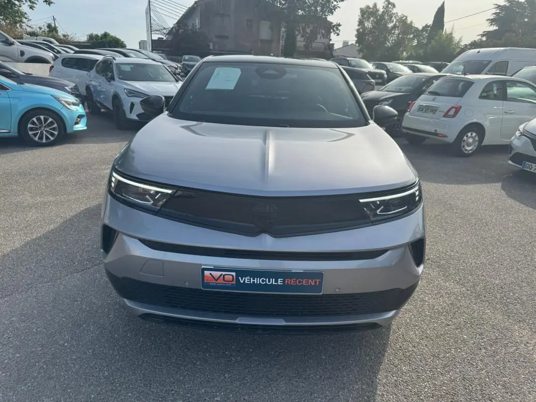 Vue frontale d'un Opel Mokka électrique gris 2025 avec calandre noire et phares LED fins, sur parking extérieur.