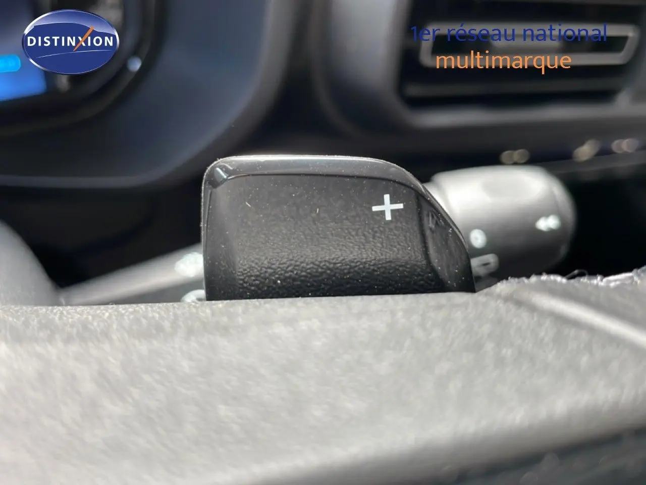 Gros plan sur la palette de changement de vitesse + au volant du Citroën Berlingo gris, intérieur noir visible en arrière-plan.