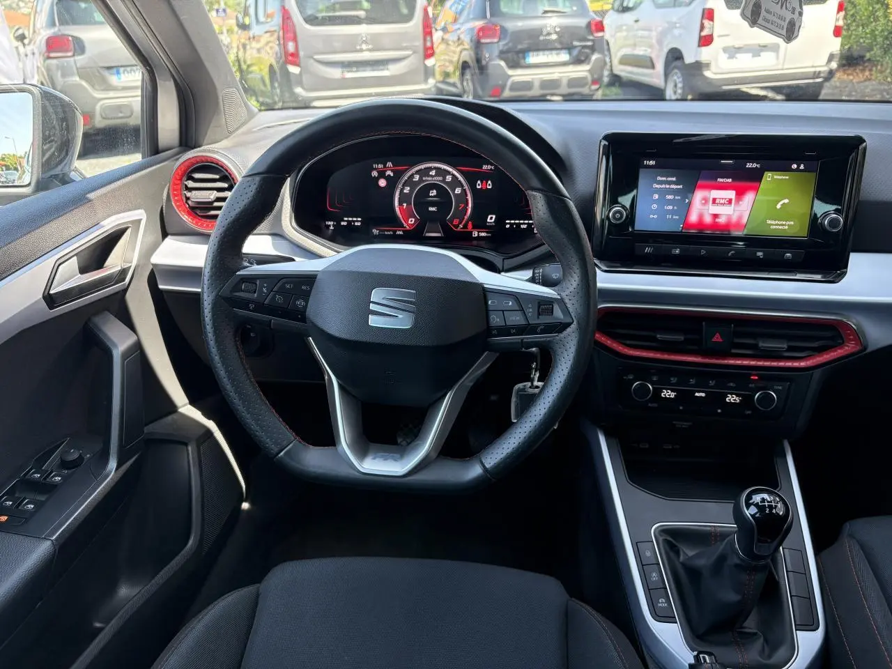 Vue intérieure frontale du volant sport cuir et tableau de bord digital du SEAT Arona 2024 avec touches rouges et levier de vitesse manuel.