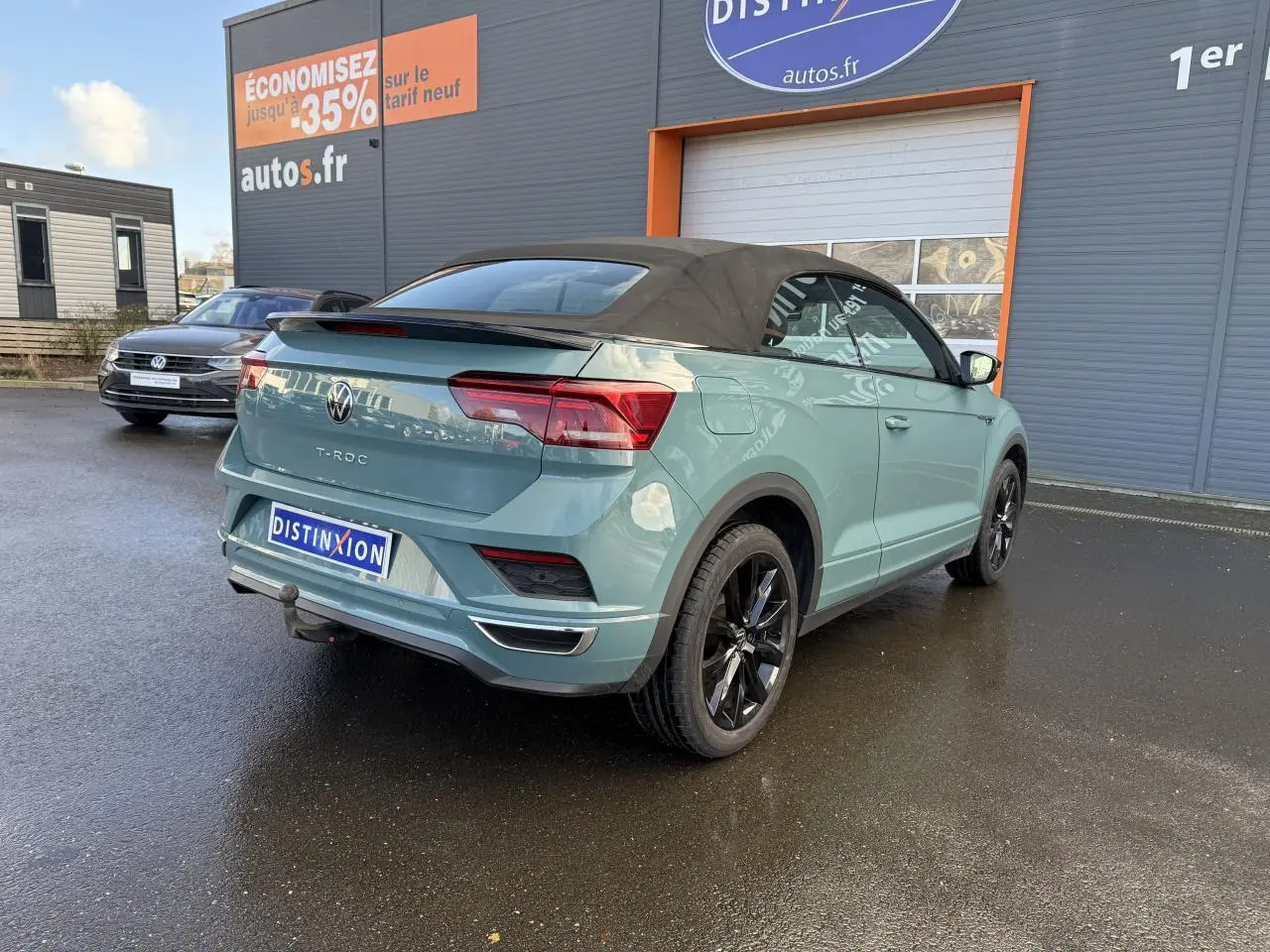 Vue 3/4 arrière d'un Volkswagen T-Roc Cabriolet vert cactus avec capote noire et attelage amovible.