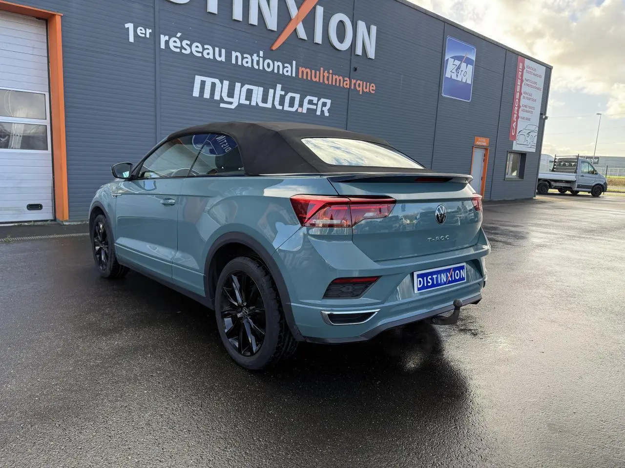 Vue 3/4 arrière droite d'un Volkswagen T-Roc Cabriolet vert cactus avec capote noire et attelage amovible.