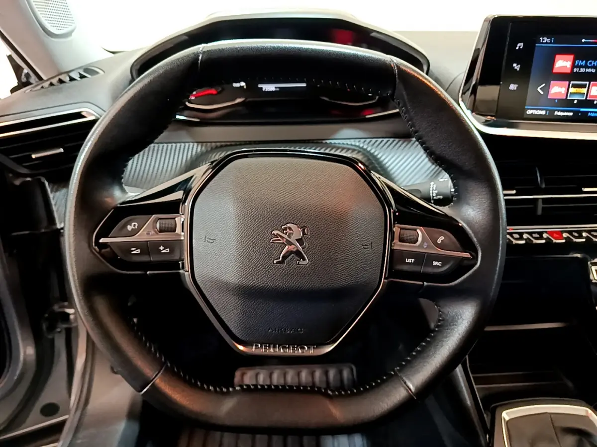 Vue rapprochée du volant cuir multifonctions noir de la Peugeot 2008, avec tableau de bord et écran tactile visibles.