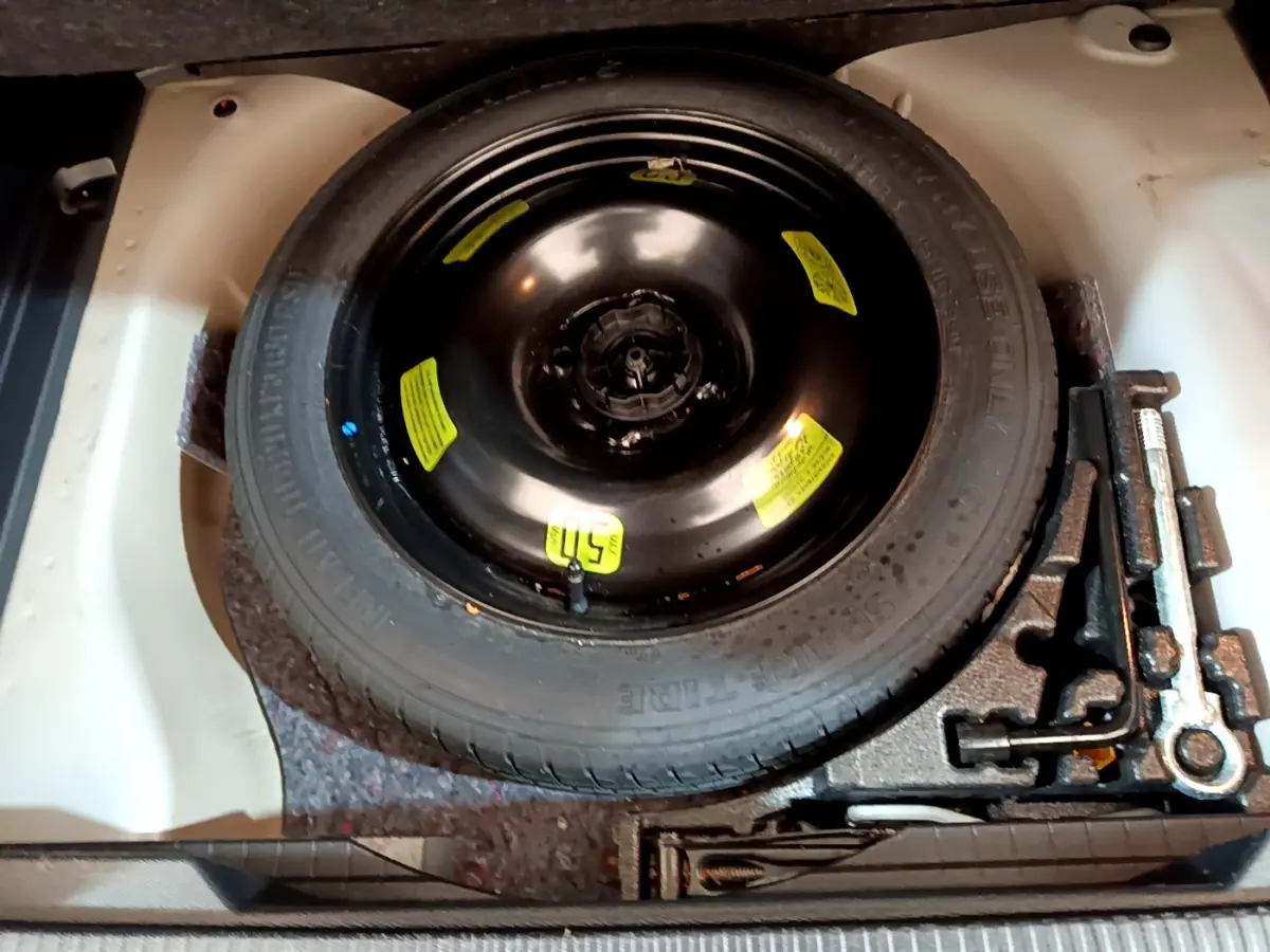 Vue plongeante sur la roue de secours noire et les outils de bord dans le coffre d'une Peugeot 2008 gris clair.