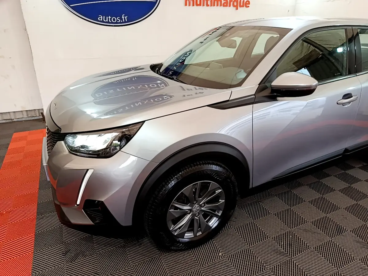 PEUGEOT 2008 gris clair en 3/4 avant gauche, avec feux LED et jantes alliage visibles sur sol intérieur.