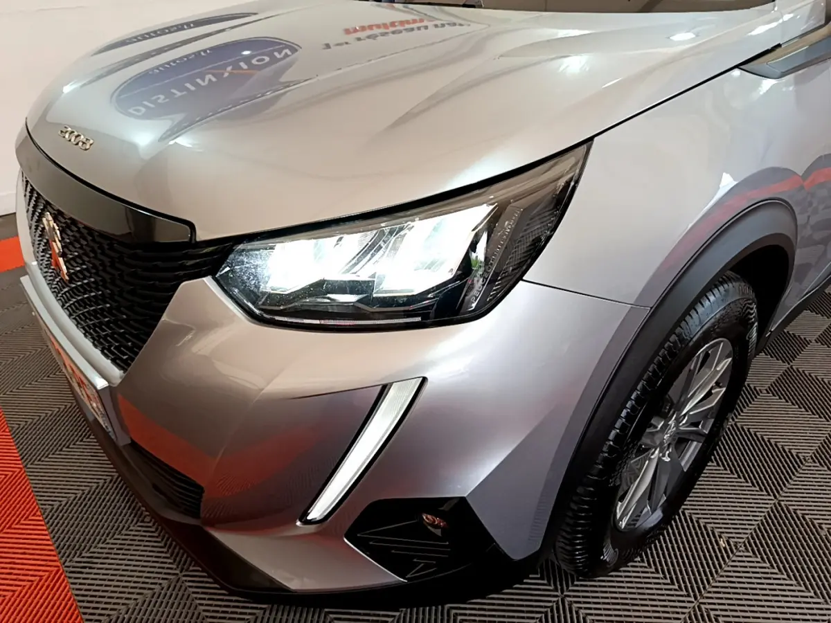 Vue 3/4 avant droit d'un Peugeot 2008 gris clair avec phares LED et calandre noire distinctive.