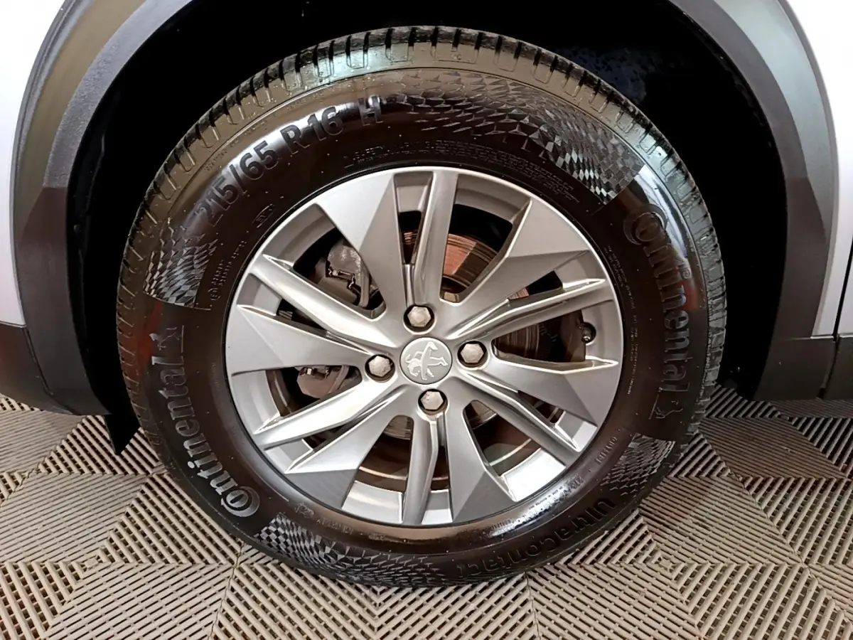 Gros plan sur la roue avant droite avec jante alliage argentée et logo Peugeot sur un Peugeot 2008 gris clair.