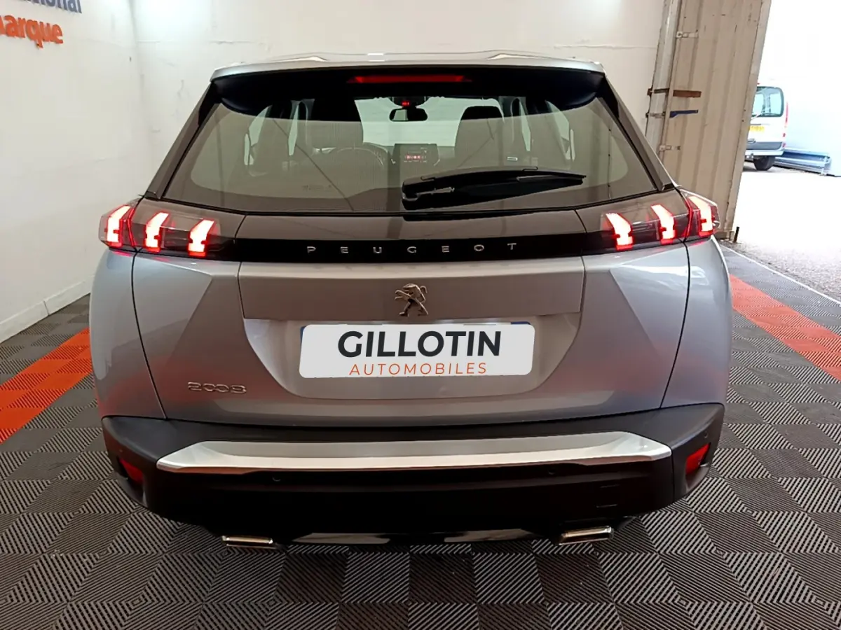 Vue arrière d'un Peugeot 2008 gris clair avec feux LED allumés dans un garage showroom.
