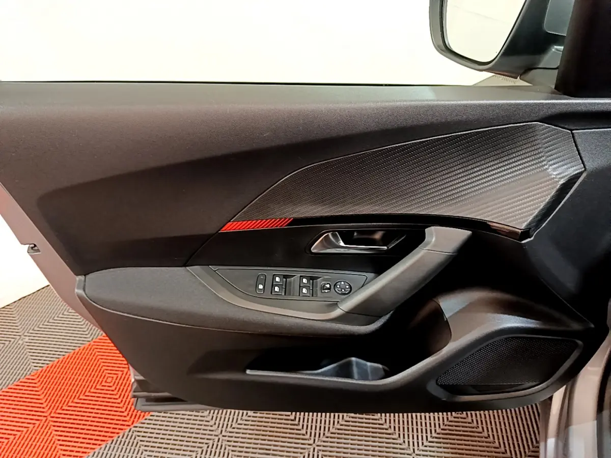 Gros plan sur la porte avant gauche du Peugeot 2008 gris clair, avec commandes électriques et insert décoratif noir texturé.